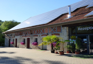 Recepción de Camping Schwabenmühle con paneles solares en el techo y macetas de flores al frente.