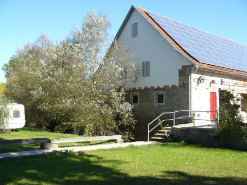 Sonniger Tag bei Camping Schwabenmühle, Solarpanels auf dem Dach, grüne Bäume und ein Wohnwagen.