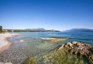 Spiaggia rocciosa e acqua limpida del Lago di Garda vicino a Vacanze col Cuore: Sivinos Camping Boutique - Glamping Gardameer.