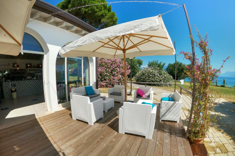 Udendørs loungemøbler under en parasol på Sivinos Camping Boutique Glamping ved Gardasøen i solskin.