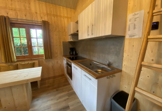 Et moderne glampingkøkken med trævægge, vindue, spisebord og stige på Camping & Chaletparc De Uitwijk.