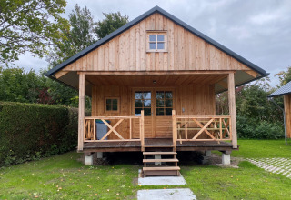 Holzhütte mit Veranda auf grünem Rasen im Camping & Chaletparc De Uitwijk – Lodges Noord-Brabant, Niederlande.