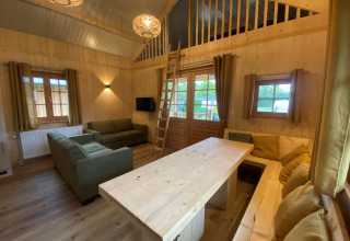 Hyggelig lodges stue med træmøbler, sofaer og hems på Camping & Chaletparc De Uitwijk i Noord-Brabant.