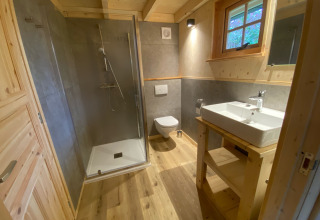 Modernes Badezimmer mit Holzdetails, großer Dusche, WC und Waschbecken in einer Glamping-Lodge in Noord-Brabant.