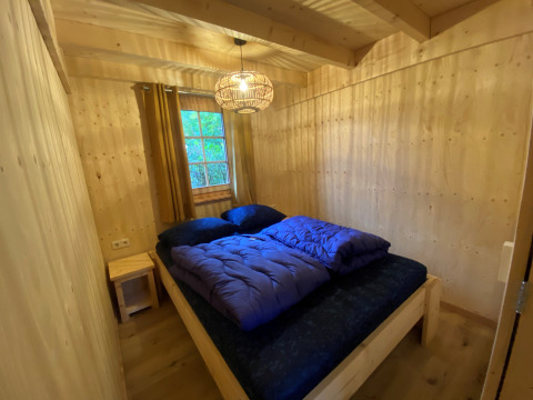 Chambre avec murs en bois, lit double et couettes bleues dans un lodge glamping à De Uitwijk, Noord-Brabant.