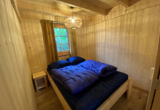 Slaapkamer met houten wanden, tweepersoonsbed en blauwe dekbedden in een glamping lodge bij De Uitwijk.