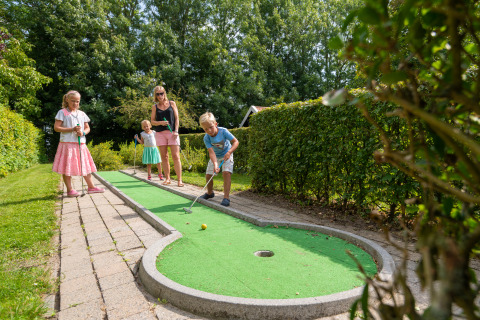 Famille jouant au mini-golf en plein air au Camping & Chaletparc De Uitwijk – Lodges Noord-Brabant en été.