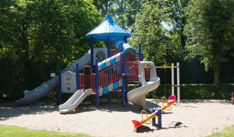 Playground with slides and seesaw surrounded by greenery at Camping & Chaletparc De Uitwijk – Lodges Noord-Brabant.