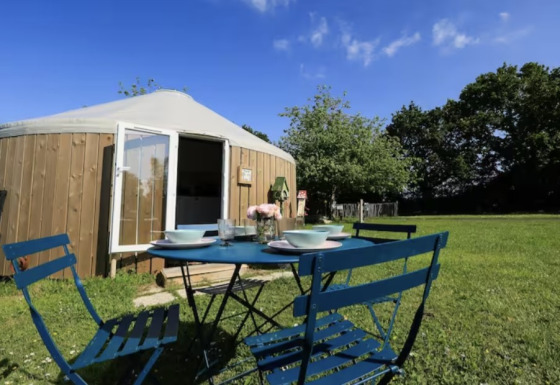 Tavolo da pranzo all'aperto davanti a una yurta glamping al Camping La Ferme de Croas Men con prato verde e alberi.