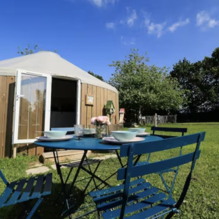 Buitenterras met tafel en stoelen voor een glamping-yurt op Camping La Ferme de Croas Men met grasveld en groen.