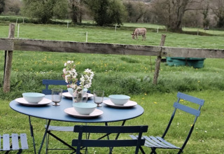 Mesa exterior puesta para cuatro junto a Camping La Ferme de Croas Men, con campo verde y burro al fondo.