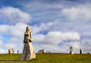 Stone sculptures on a grassy field under a blue sky at Camping La Ferme de Croas Men glamping site.