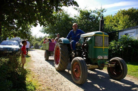 Families enjoy a tractor wagon ride at Camping La Ferme de Croas Men, surrounded by greenery and sunshine.