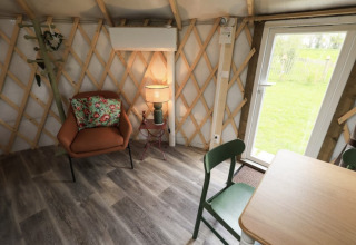 Intérieur confortable de glamping au Camping La Ferme de Croas Men avec fauteuil, table, et vue sur le jardin.