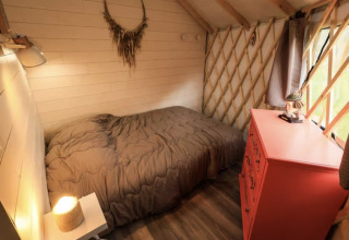 Knusse kamer met bed, grijs dekbed, rode ladekast en raam bij Camping La Ferme de Croas Men glamping.