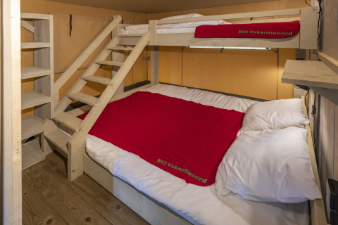 Alloggio glamping Bio Vakantieoord Veluwe con letto matrimoniale, letto a castello e coperte rosse.