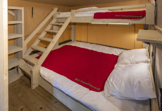 Alloggio glamping Bio Vakantieoord Veluwe con letto matrimoniale, letto a castello e coperte rosse.