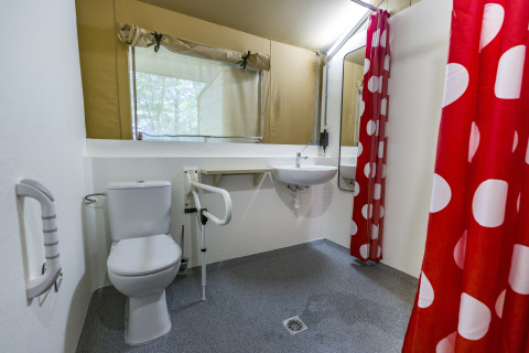 Toegankelijke badkamer in een glampingtent bij Bio Vakantieoord - Glampingtenten Veluwe, met rood gordijn met stippen.