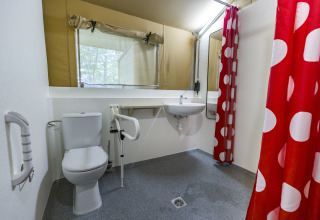 Baño accesible en tienda glamping de Bio Vakantieoord - Glampingtenten Veluwe, con cortina roja de lunares.