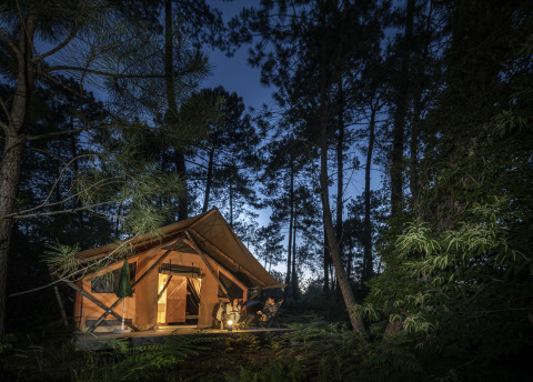 Vue nocturne d'une tente glamping dans la forêt à Huttopia Landes Sud - Glamping Aquitaine, entrée éclairée.