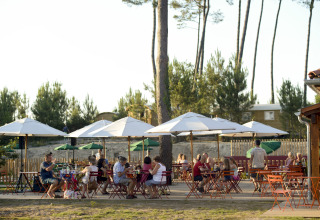 Buiten eetgedeelte met parasols en gasten bij Huttopia Landes Sud - Glamping Aquitaine in Frankrijk.