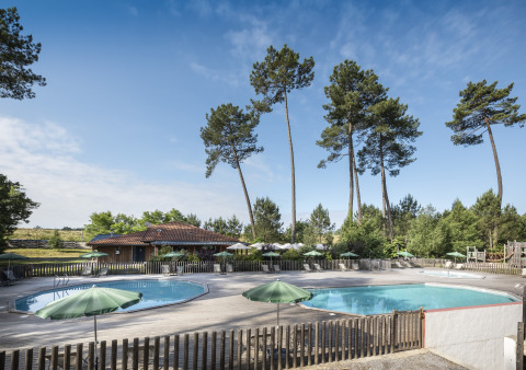 Buitenzwembad met parasols en hoge bomen bij Huttopia Landes Sud - Glamping in Aquitaine, Frankrijk.