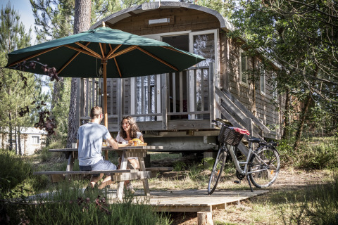 Two people enjoy breakfast at a table outside a cabin at Huttopia Landes Sud - Glamping Aquitaine.