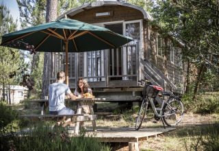 Twee mensen ontbijten aan een picknicktafel voor een hut bij Huttopia Landes Sud - Glamping Aquitaine.