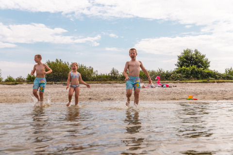 Niños juegan y salpican en el agua en la playa del Vakantiepark IJsselhof - Safarilodges Noord-Holland.