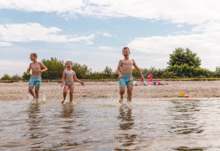 Kinderen spelen en spatten in het water op het strand bij Vakantiepark IJsselhof - Safarilodges Noord-Holland.