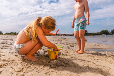 Dos niños juegan en la arena de la playa en Vakantiepark IJsselhof - Safarilodges Noord-Holland.