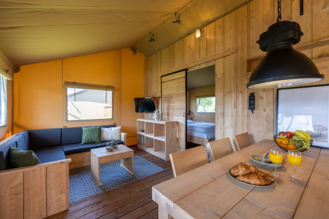 Vista interior de alojamiento glamping en Vakantiepark IJsselhof - Safarilodges Noord-Holland con mobiliario de madera.
