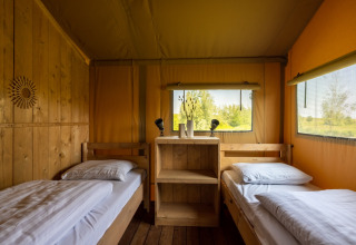 Interieur van een glamping safarilodge op Vakantiepark IJsselhof met twee bedden en uitzicht buiten.