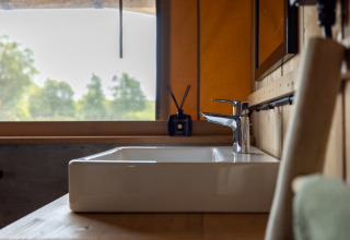 Lavabo moderne et robinet dans une safarilodge au Vakantiepark IJsselhof, vue sur la nature par la fenêtre.