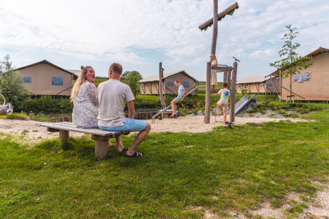 Famille profitant du glamping à Vakantiepark IJsselhof - Safarilodges Noord-Holland avec aire de jeux.