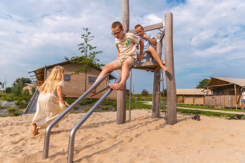 Kinderen spelen op een houten glijbaan in het zand voor glampingtenten op Vakantiepark IJsselhof, Nederland.