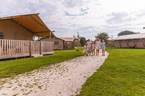 Gezin wandelt op grindweg tussen safaritenten op Vakantiepark IJsselhof Safarilodges, Noord-Holland.