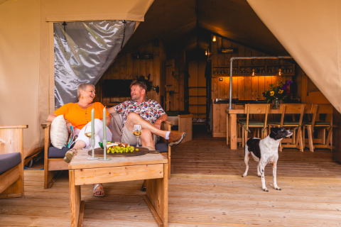 Couple détendu devant une safarilodge de glamping avec leur chien au Vakantiepark IJsselhof, Noord-Holland.