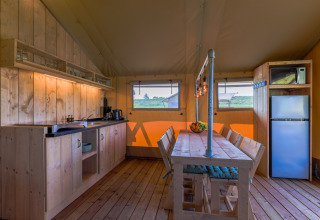 Interior de una lodge safari en Vakantiepark IJsselhof con cocina, mesa de comedor y ventanas panorámicas.