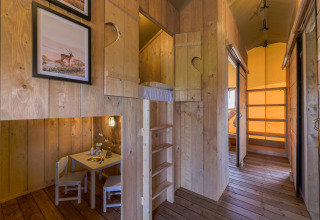 Interieur van een gezellige houten safarilodge met stapelbedden en kinderhoek bij Vakantiepark IJsselhof.