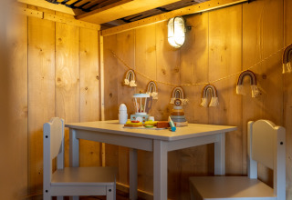 Gemütlicher Kinderbereich mit Holzwänden, kleinem Tisch, Stühlen und Spielzeug in einer Safarilodge.