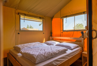 Binnenkant van een safarilodge met dubbel bed, ramen en zonlicht in Vakantiepark IJsselhof, Noord-Holland.