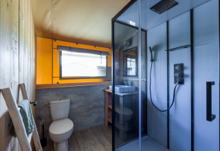 Moderne badeværelse i en safarilodge på Vakantiepark IJsselhof, med brusekabine, toilet og vindue.