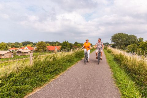 Two people cycling on a path near glamping at Vakantiepark IJsselhof Safarilodges, North Holland, Netherlands.