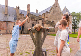 Kinderen spelen met een middeleeuwse schandpaal op de binnenplaats van Vakantiepark IJsselhof in Noord-Holland.