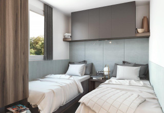 Hébergement glamping moderne avec deux lits simples, placards gris et déco chaleureuse lumineuse.