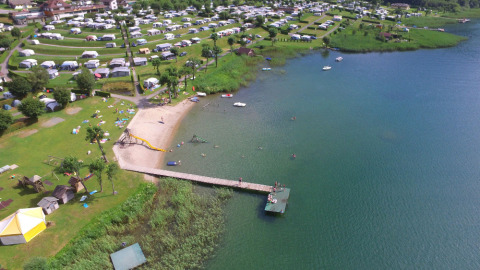 Luchtfoto van Terrassencamping Ossiacher See met glampingplekken, zandstrand en pier aan het meer.