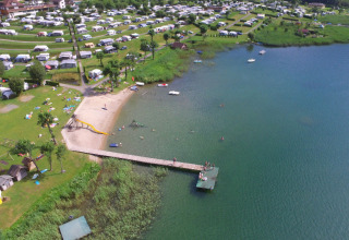 Vista aerea di Terrassencamping Ossiacher See con glamping, spiaggia sabbiosa e pontile sul lago.