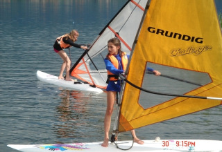 Twee kinderen windsurfen op het meer bij Terrassencamping Ossiacher See - Stacaravans Karinthië in Oostenrijk.