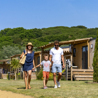En familie går foran glampinghytter omgivet af natur på Camping Saint Pabu Plage - Glamping Bretagne.